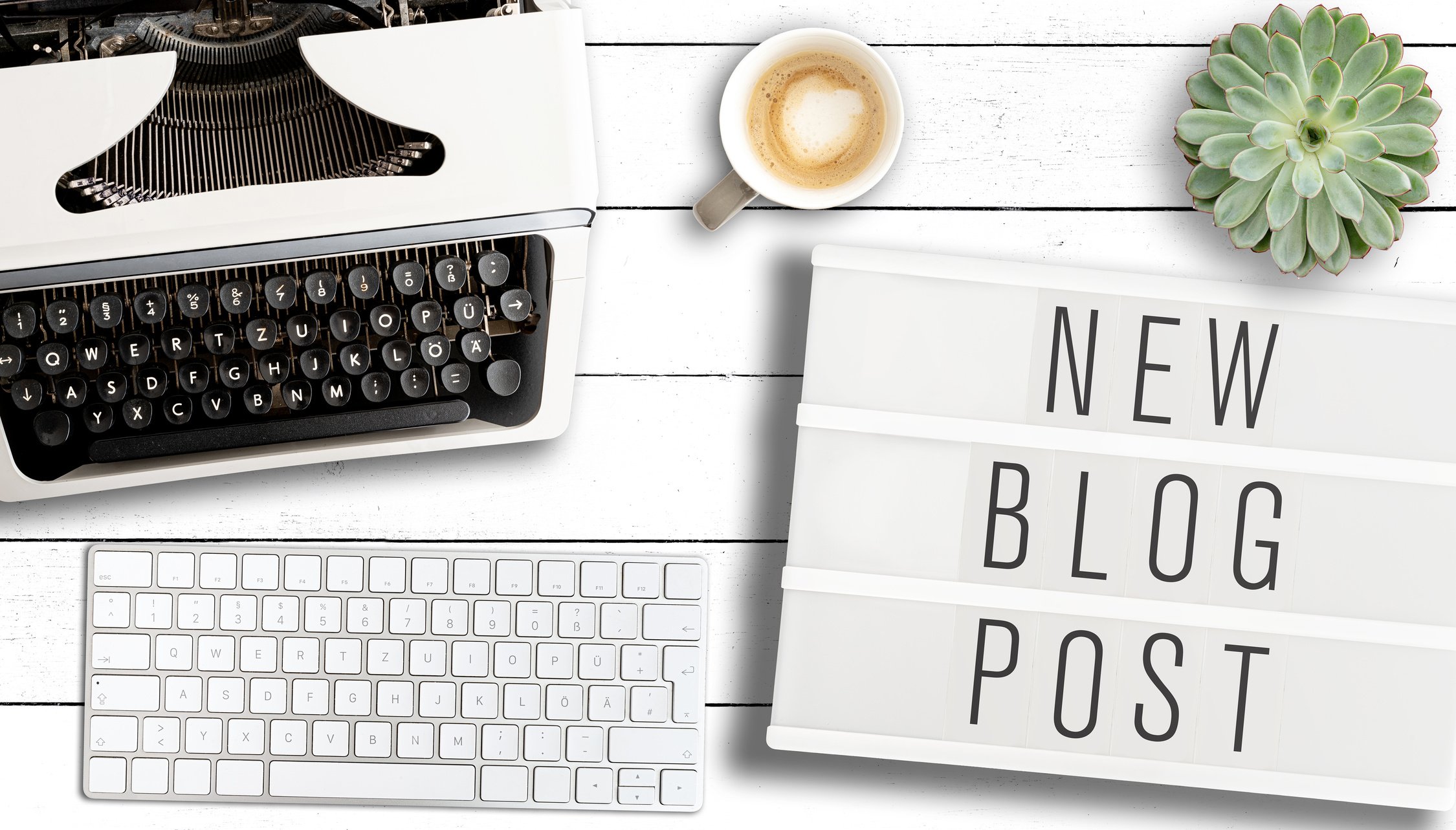 text NEW BLOG POST on light box on table with old typewriter, computer keyboard and cup of coffee